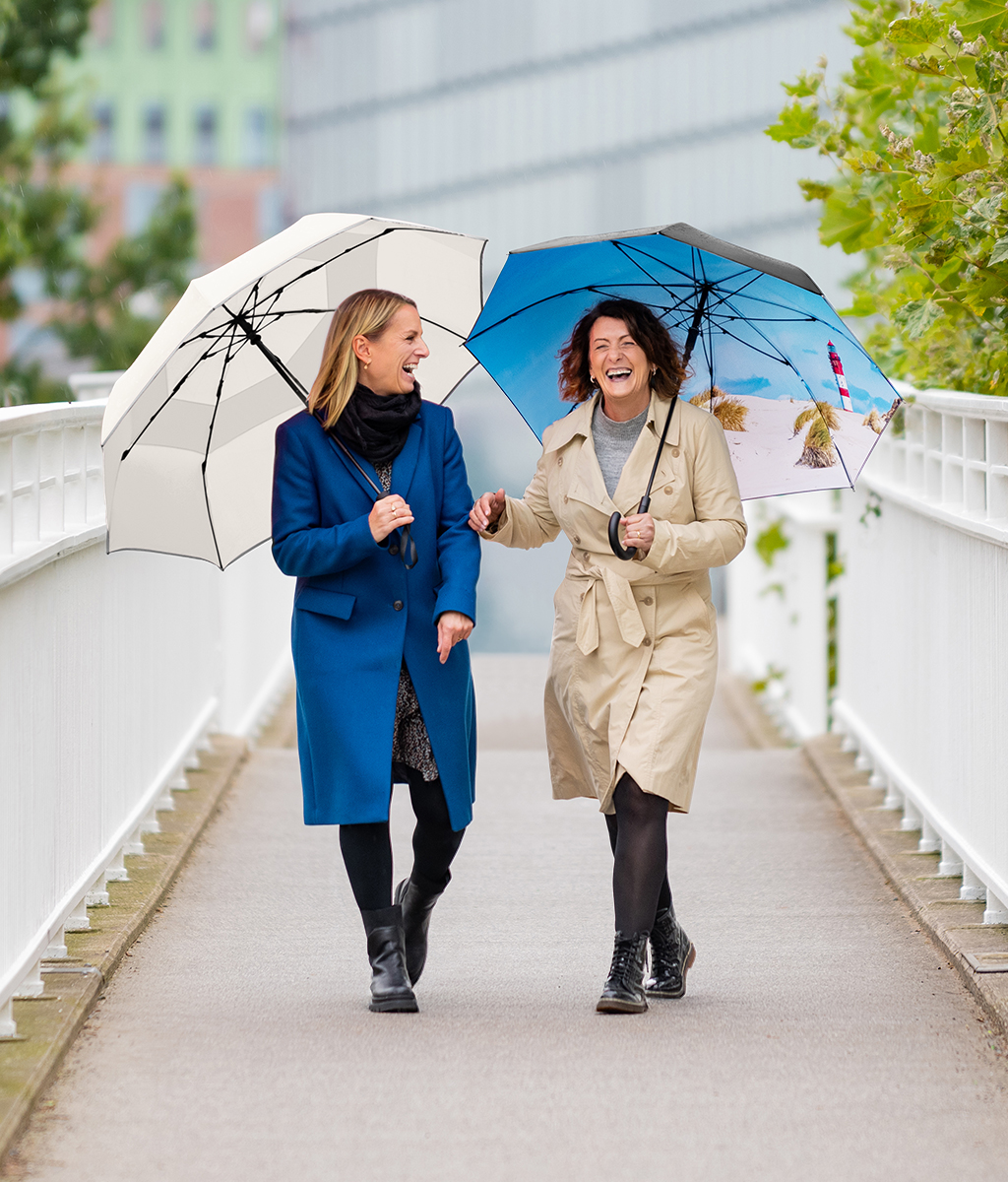 Two laughing women with umbrellas on a bridge