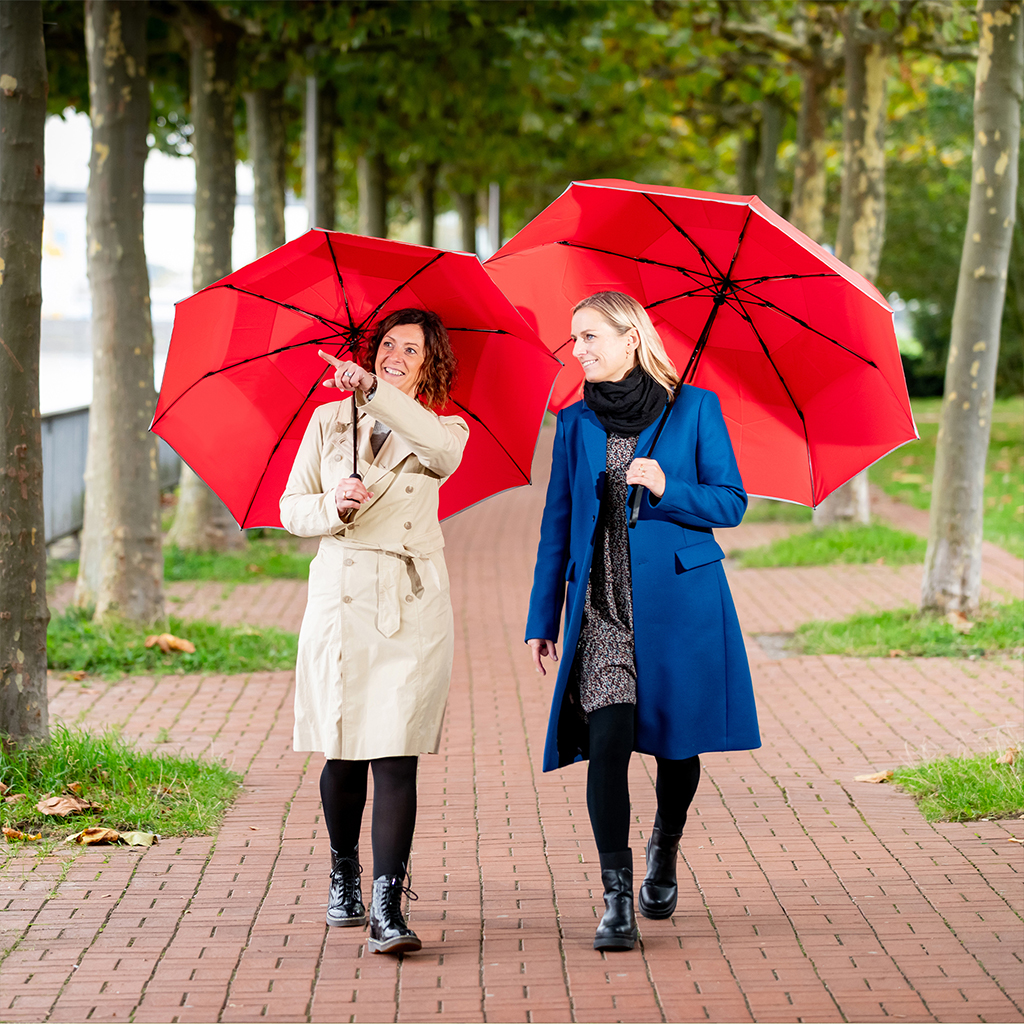 Two women with umbrellas under an alley of trees